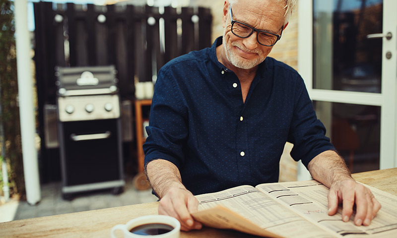 man on his porch reading the paper and drinking a cup of coffee safe retirement income